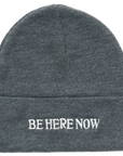 Gray beanie with 'BE HERE NOW' text on a white background