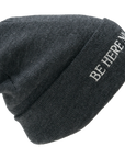 Gray beanie with 'BE HERE NOW' text on a white background