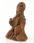 A figurine of a seated, kneeling deity or saint with ornate crown and robe details, photographed on a clean white background.