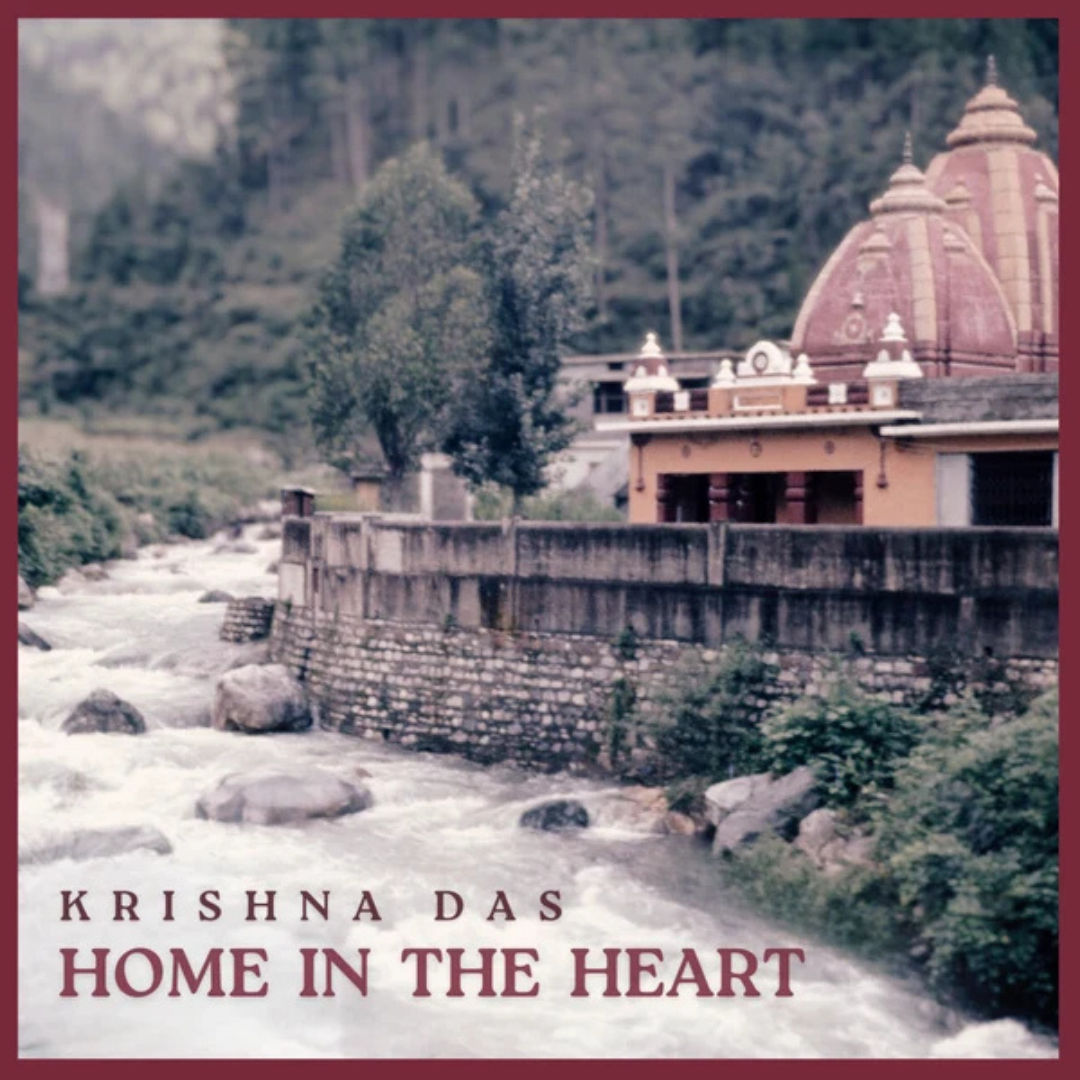 A square promotional image with a red border and overlaid text reading 'KRISHNA DAS HOME IN THE HEART' at the bottom. The scene shows a river flowing in the foreground, stone walls, trees, and a temple-like building with domes in the background.