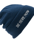 Blue beanie with 'BE HERE NOW' text on a white background