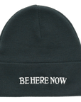 Black beanie with 'BE HERE NOW' text on a white background