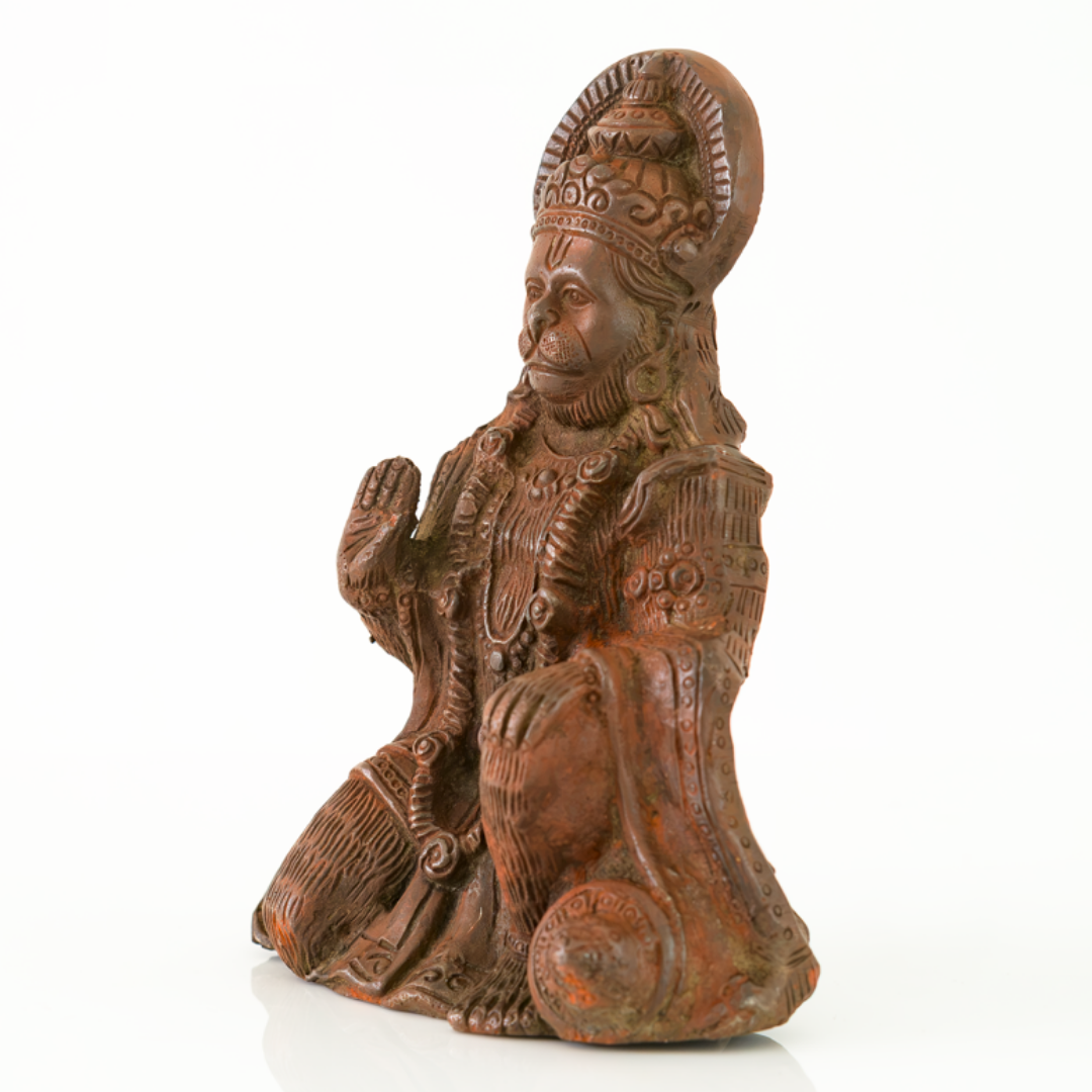 A figurine of a seated, kneeling deity or saint with ornate crown and robe details, photographed on a clean white background.
