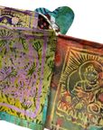Two folded hand-woven fabric prayer flags with traditional Indian motifs, featuring metallic gold foil printing on a green, purple, and orange base.
