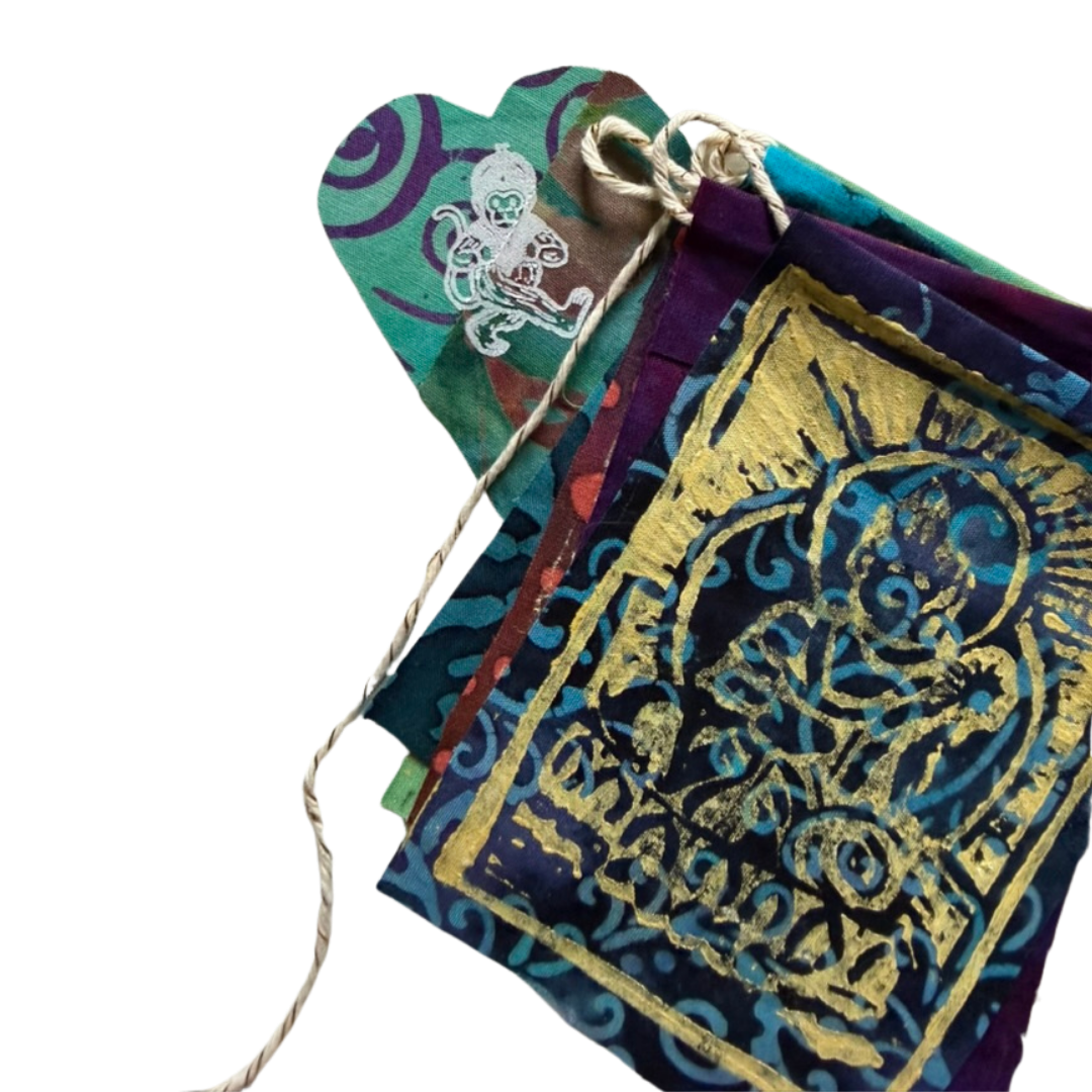 A close-up of a multicolored fabric pouch or bookmark with a rustic twine loop, featuring a prominent gold foil stamp design on a dark blue background.