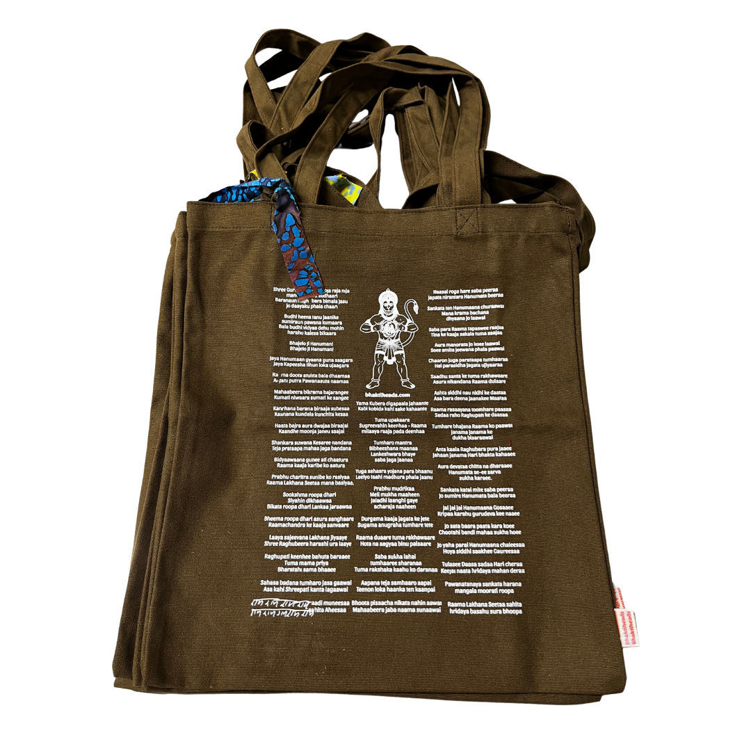 An olive brown canvas tote bag featuring a white graphic print of a skeleton character surrounded by text, with a blue patterned tag attached near the handles.