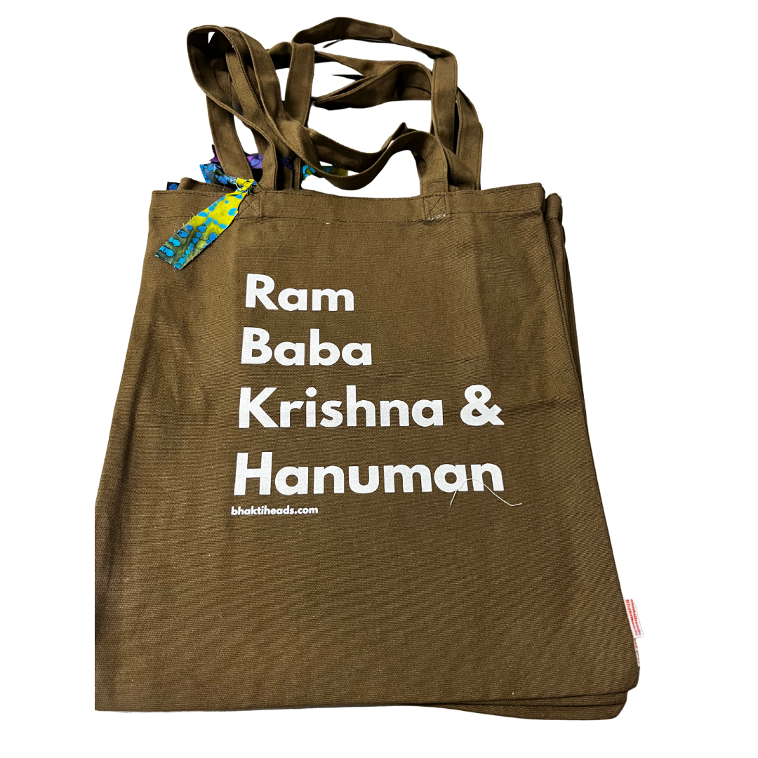 A brown canvas tote bag with white printed text reading 'Ram Baba Krishna &amp; Hanuman' and a small 'bhaktihoods.com' URL near the bottom.
