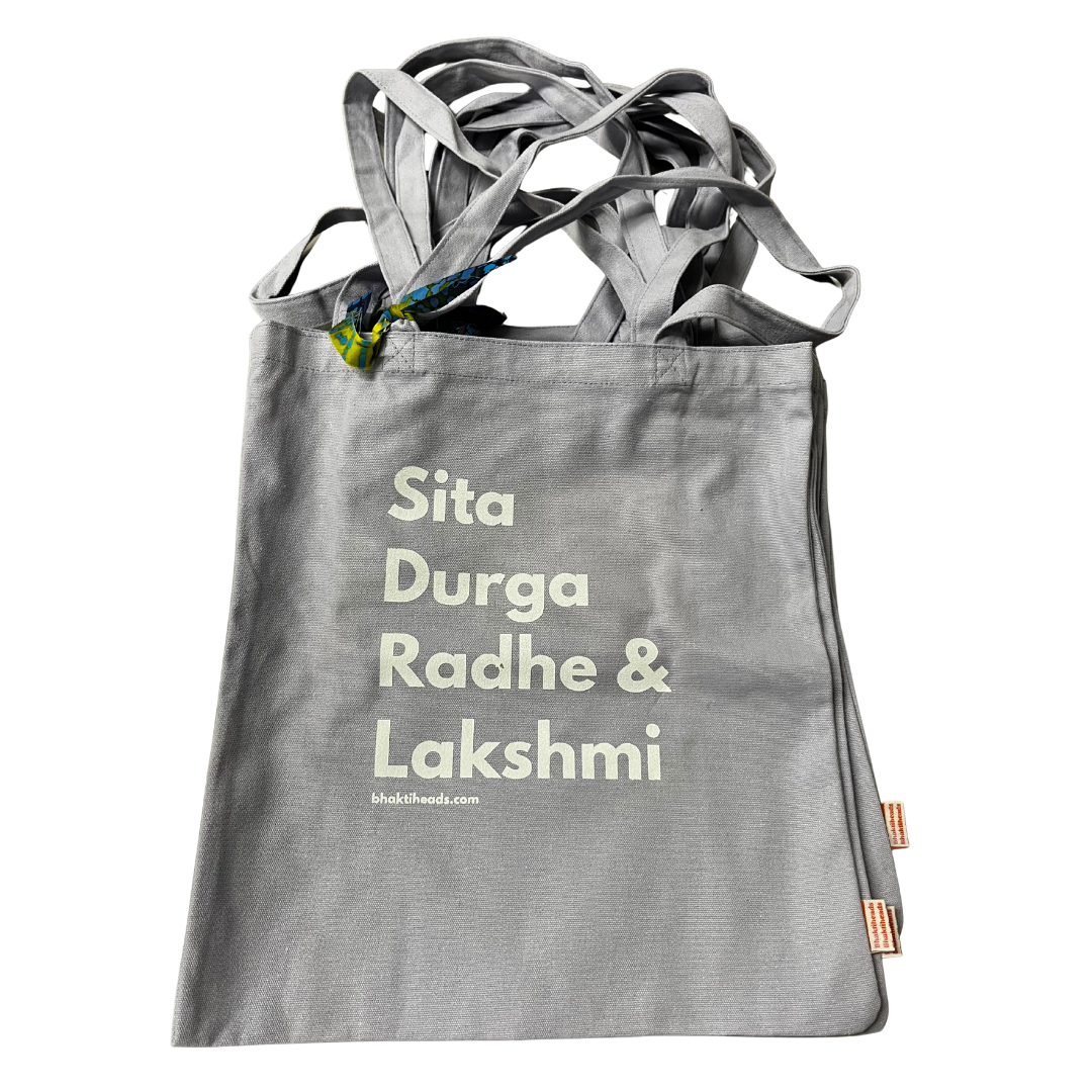 A gray canvas tote bag with four shoulder straps, featuring the names 'Sita Durga Radhe &amp; Lakshmi' printed in a light cream-colored serif font. The brand name 'whatthetheweek.