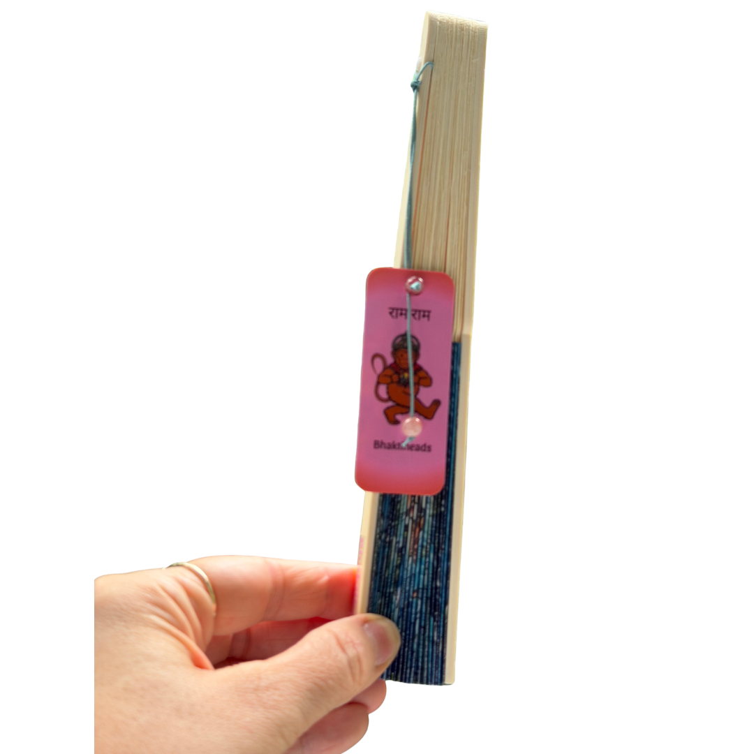 A hand holding a slim, open book or notebook with cream-colored pages and a pink bookmark tag attached. The bookmark tag features a cartoon monkey and the text 'Ram Ram' and 'BookCasts'.