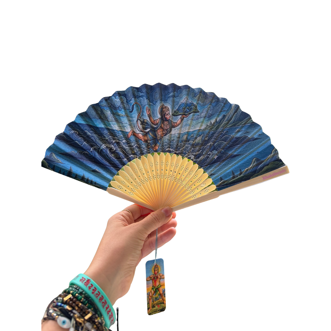 A hand holds a folding hand fan with a blue illustrated design depicting a figure on a wave, with a yellow-gold handle. A matching card tag hangs from the handle, and the background is solid white.